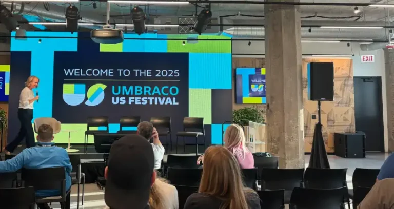 A stage with Umbraco branding on a big screen. A woman is getting on stage from the left.